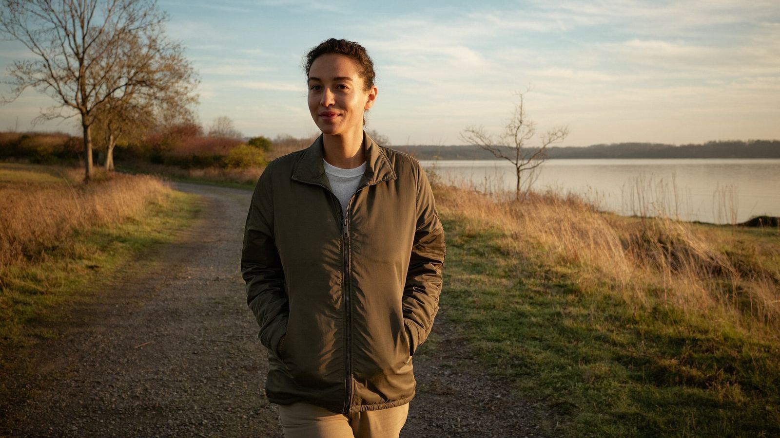 Woman walking alone on a quiet trail along a Great Lakes shoreline in early morning sunlight, part of a circadian rhythm recovery routine