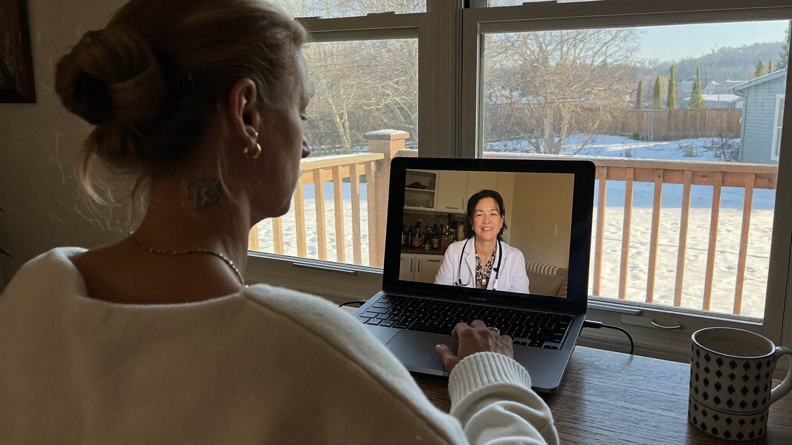 Woman on a telehealth video consultation at her kitchen table in a Michigan home, discussing her symptoms with a healthcare provider